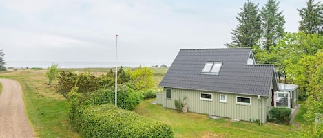 A single-story house with a sloped roof, a small attached shed, and a flagpole.