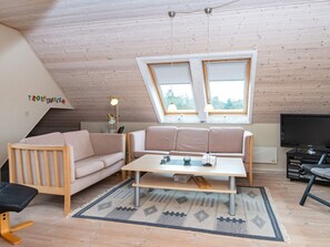 A loft-style living room with a sloped ceiling, a sofa, a coffee table, a television, and a small wooden bench. - Spacious Holiday Home in Hemmet near Sea (Hemmet)