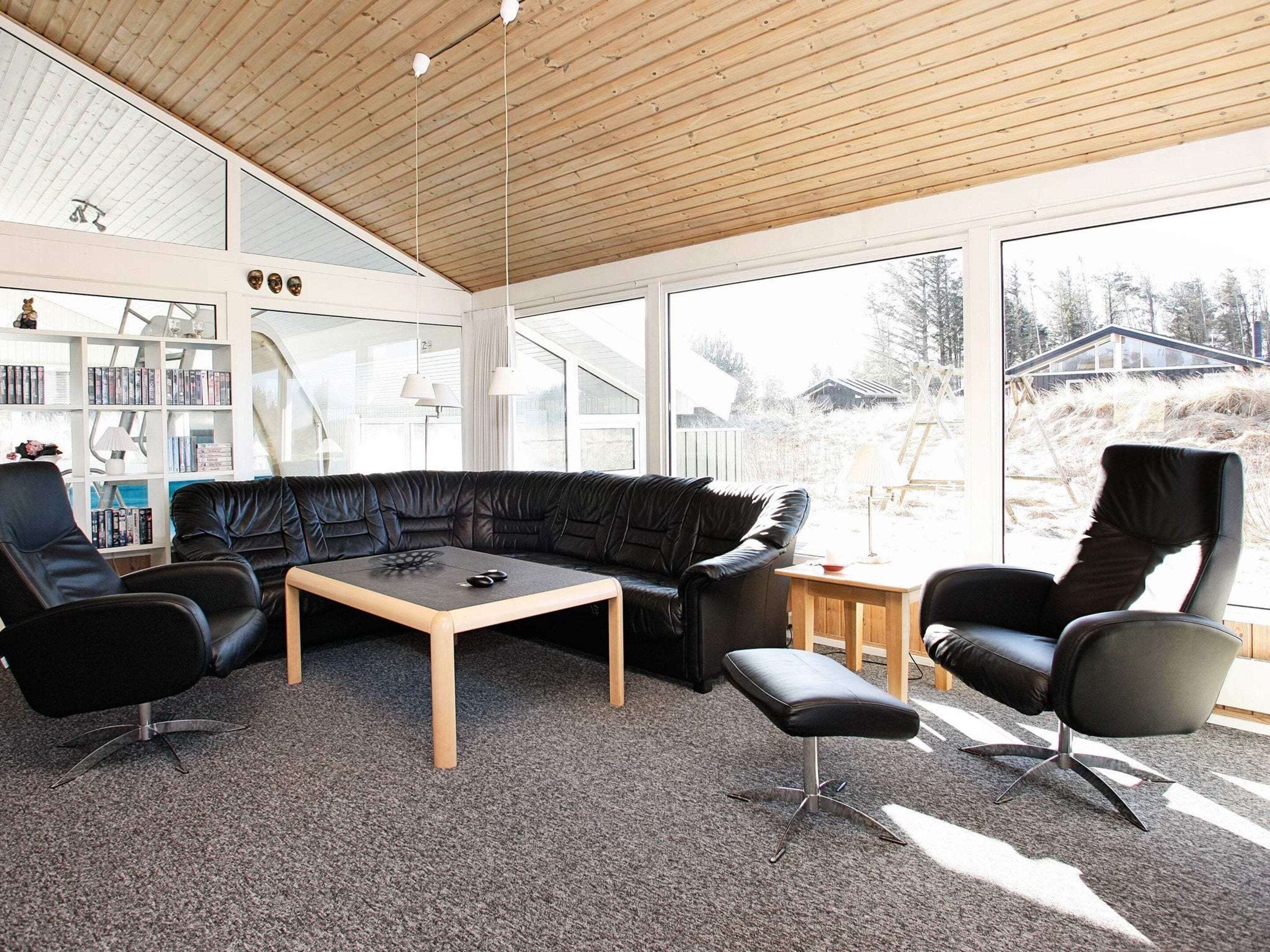 Ett modernt vardagsrum med en svart lädersoffa, ett soffbord i trä och svarta läderstolar.