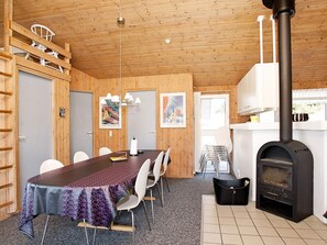 A wooden interior with a dining table, chairs, a fireplace, and a ladder.