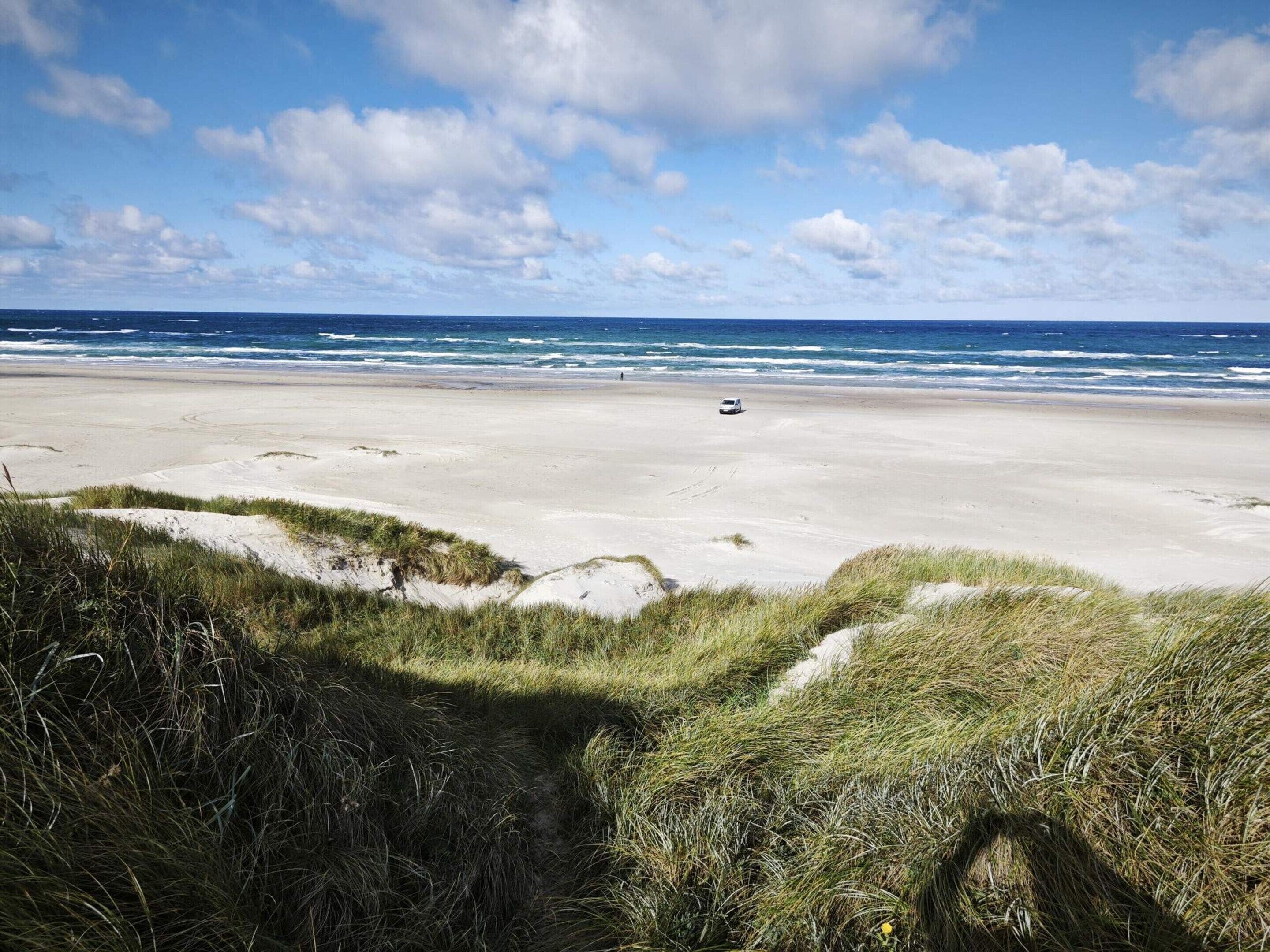 A beach with sand dunes and a vehicle on the beach.