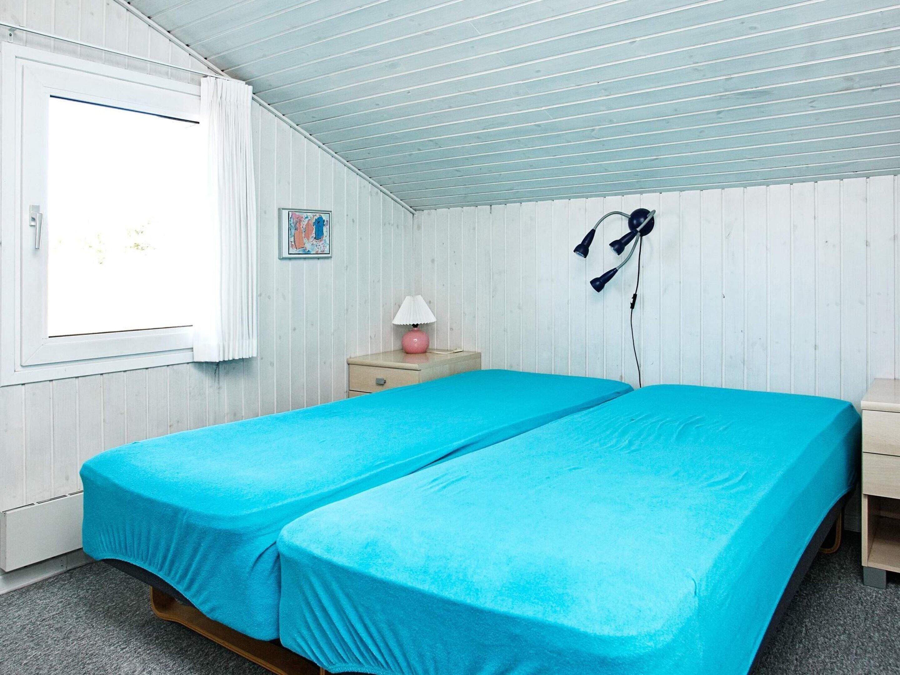 A room with two beds, a window, a nightstand, a lamp, and a wall-mounted hairdryer.