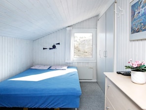 A room with a bed, a window, a wall-mounted lamp, a radiator, a dresser, and a potted plant. - 5 Star Holiday Home in Blokhus (Blokhus)
