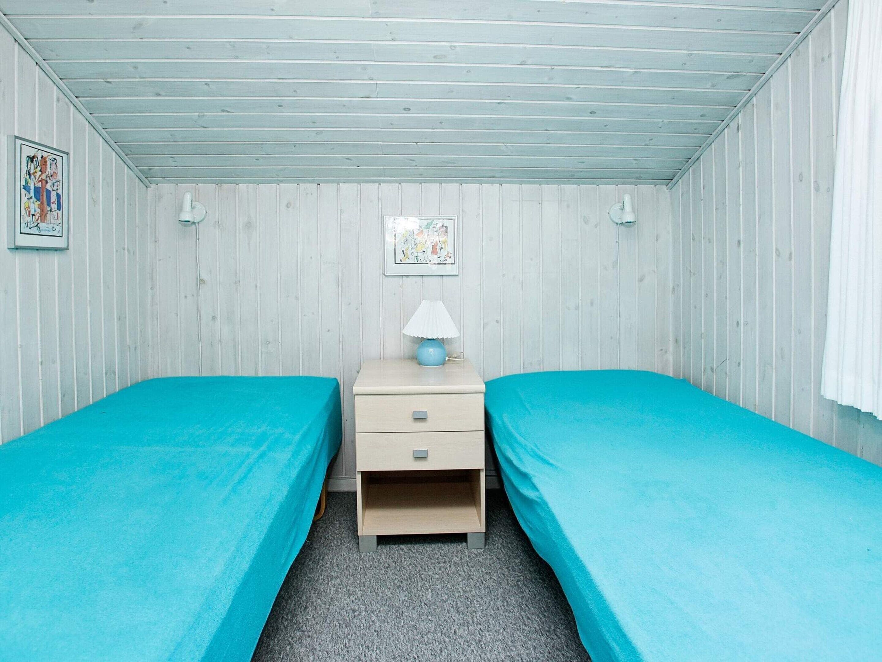 A room with two single beds, a nightstand with a lamp, and a wall-mounted picture.