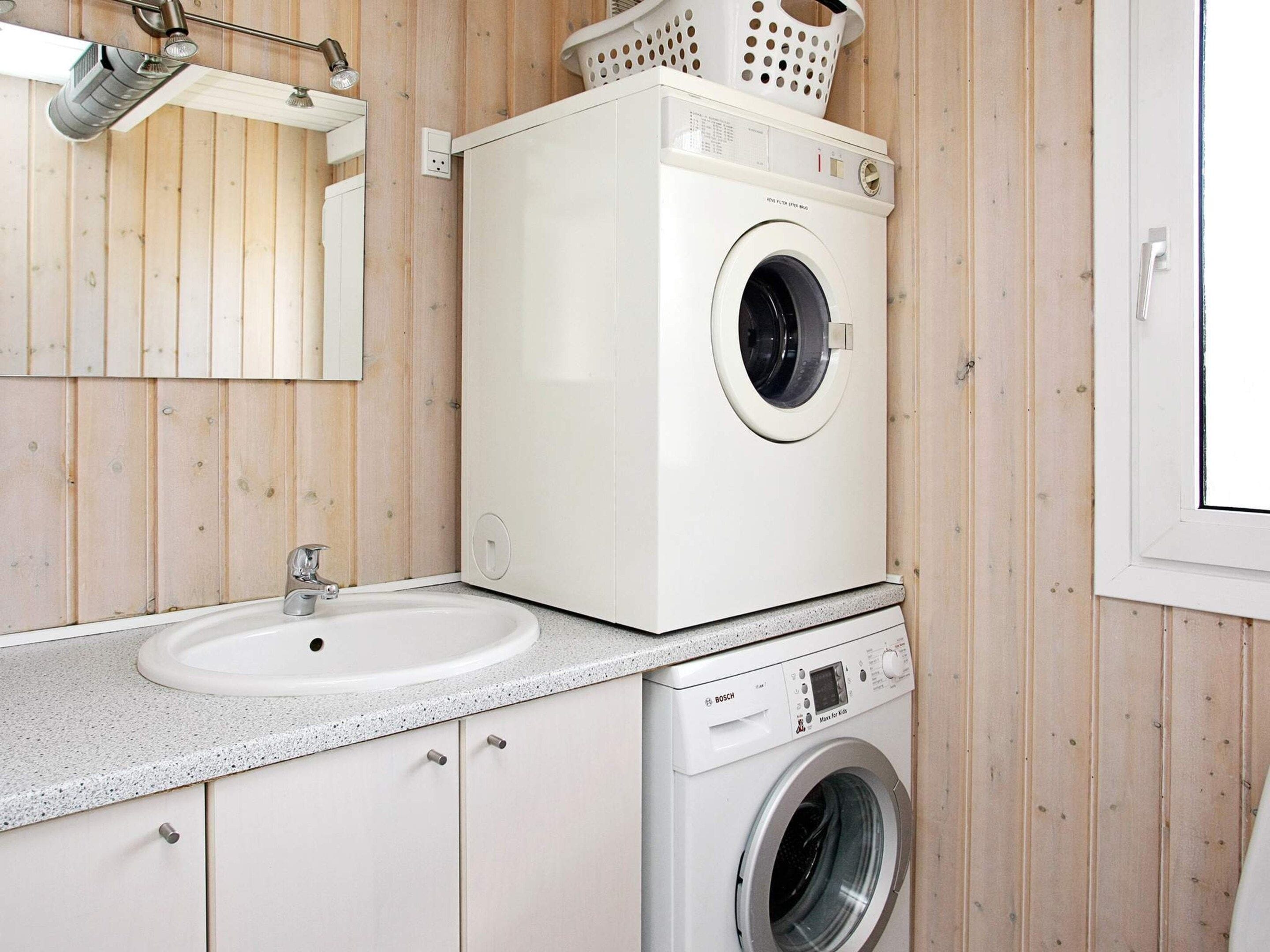 A compact laundry room with a washing machine, a sink, and a mirror.