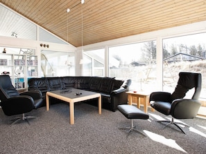 A modern living room with a black leather sofa, a wooden coffee table, and a black leather armchair. There is a bookshelf filled with books and decorative items.
