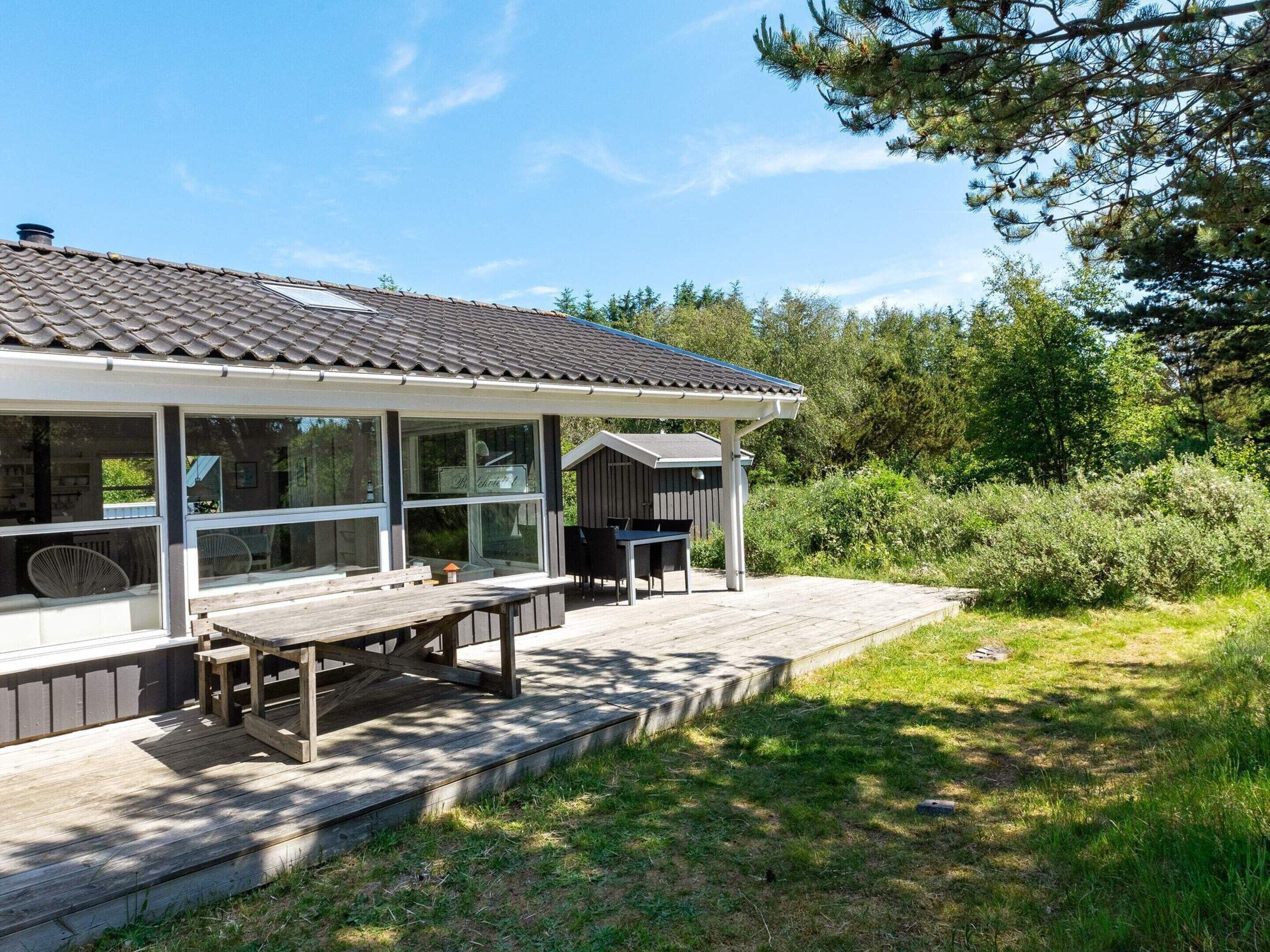 Ein Haus mit überdachter Terrasse, Sitzgelegenheit im Freien und Blick auf die umliegende Natur.