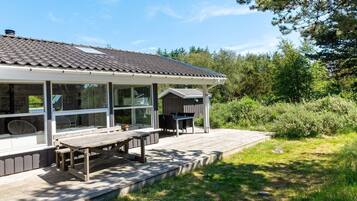 Ein Haus mit überdachter Terrasse, Sitzgelegenheit im Freien und Blick auf die umliegende Natur.