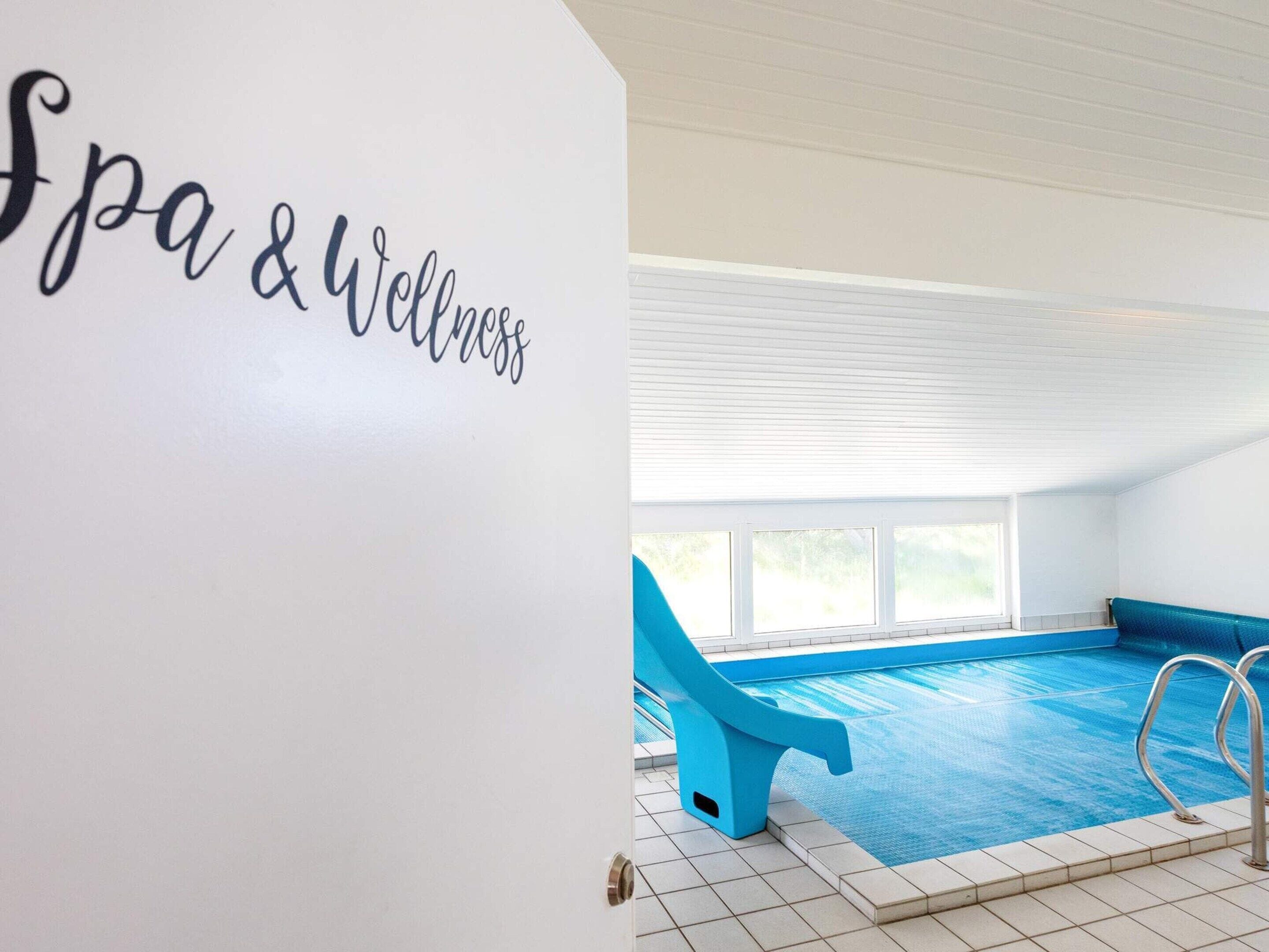 An indoor swimming pool with a blue chair and a sign reading 'Spa & Wellness'.
