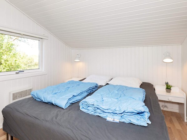 A bedroom with a bed, two bedside tables, a window, and a potted plant.