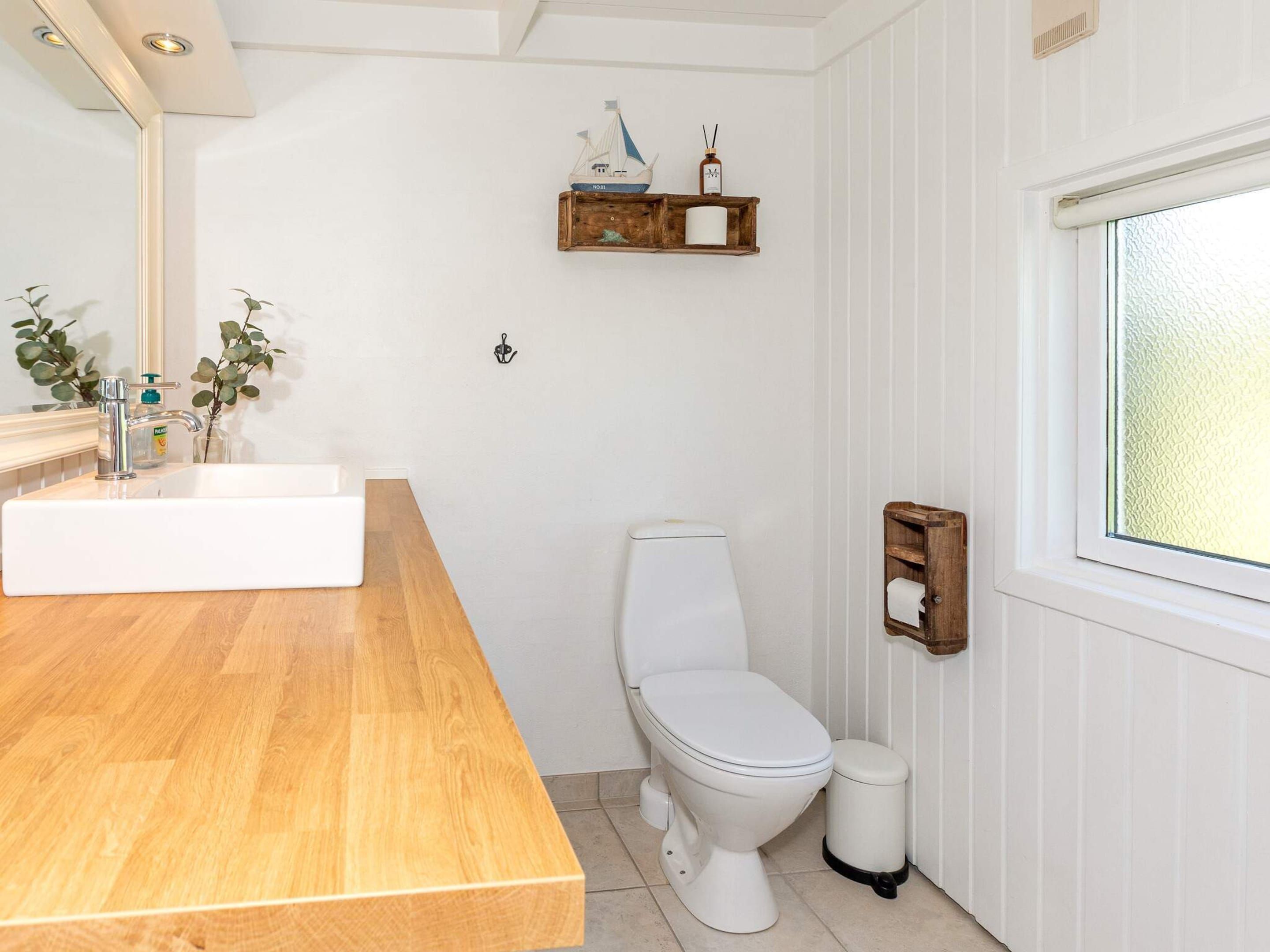 A bathroom with a wooden vanity, white toilet, and a window with frosted glass.