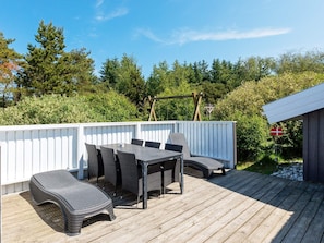 Eine Terrasse im Freien mit Tisch und Stühlen, umgeben von einem weißen Zaun, mit Bäumen und einer Flagge im Hintergrund.
