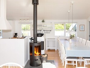 Moderni keittiö, jossa on puukamiina, valkoiset kaapit ja ruokailutila, jonka pöydällä on raidallinen pöytäliina.