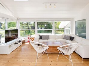 Un salon spacieux avec un grand canapé blanc, deux fauteuils blancs, une table basse en bois et un téléviseur à écran plat.
