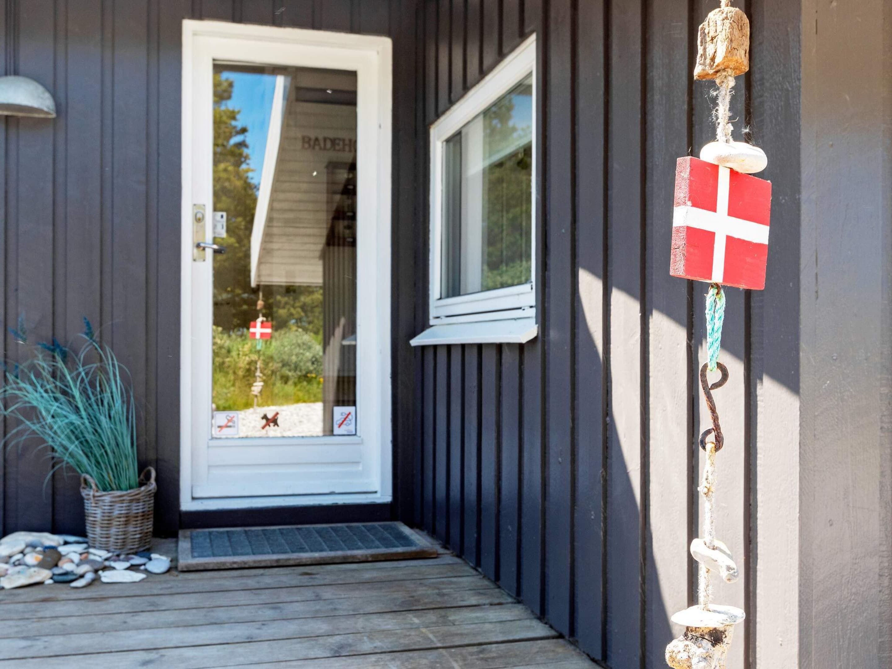 Eine Holztür mit Fenster, eine kleine Veranda mit Fußmatte und eine Flagge an der Wand.