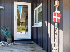 Une porte en bois avec une fenêtre, un petit porche avec un paillasson et un drapeau accroché au mur.