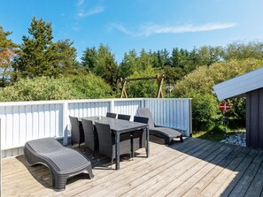 Une terrasse extérieure avec une table et des chaises, entourée d’une clôture blanche et de verdure.
