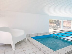A swimming pool with a blue interior, white walls, and a white chair.
