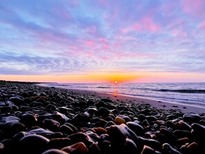 Une plage au coucher du soleil, avec des galets et l’océan.