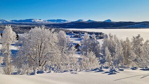 A snow-covered landscape with a cabin in the foreground and mountains in the background. - 6 Person Holiday Home in Nordli (Lierne)