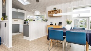 Une cuisine moderne avec des meubles blancs, un îlot central et des chaises bleues disposées autour d’une table à manger.