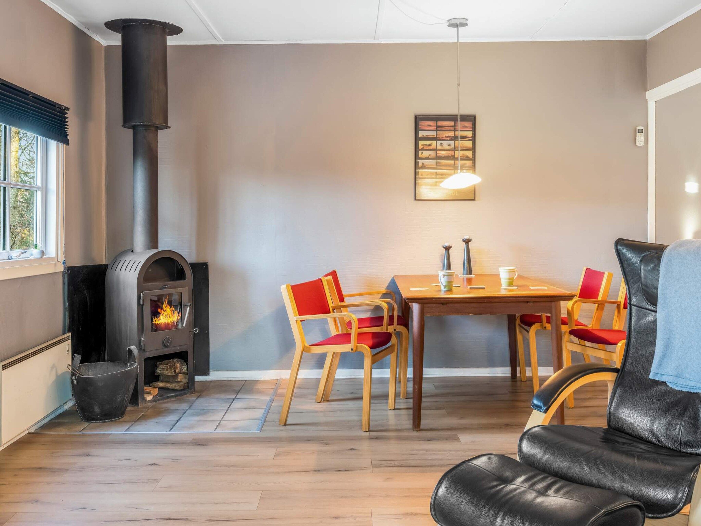 A room with a wood-burning stove, a dining table with chairs, and a window with blinds.