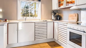 A modern kitchen with white cabinetry, a window with a view of trees, a built-in oven, and a coffee maker. - 4 Person Holiday Home in Skaerbaek (Skaerbaek)