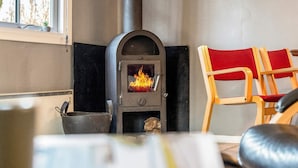 A cozy room with a wood-burning stove, a window with a view, and a red chair. - 4 Person Holiday Home in Skaerbaek (Skaerbaek)