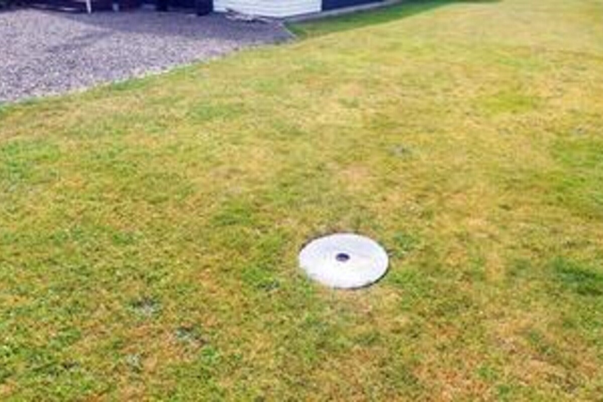 A grassy area with a circular object, possibly a manhole cover, in the center.
