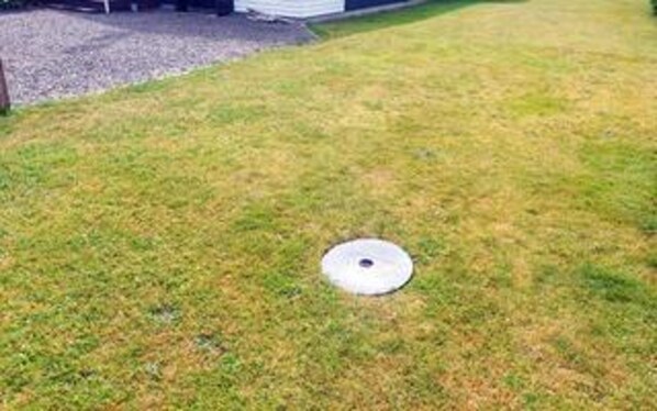 A grassy area with a circular object, possibly a manhole cover, in the center. - 5 Star Holiday Home in Vaeggerlose (Vaeggerlose)