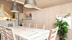 Un coin repas avec une table recouverte d’un papier décoratif imprimé façon journal, des chaises en bois, un luminaire suspendu et une plante en pot.