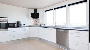A modern kitchen with white cabinets, a black microwave, a coffee maker, and a dishwasher. - 10 Person Holiday Home in Rodby-by Traum (Rodby)