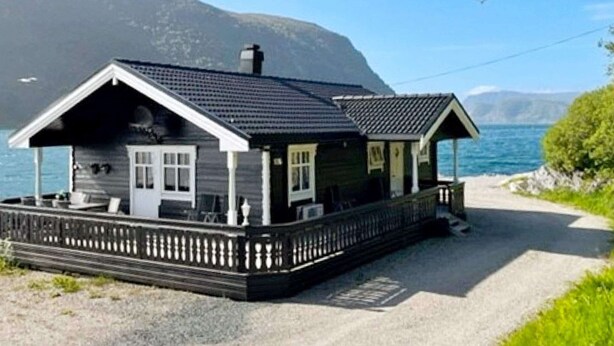 A wooden cabin with a porch, located near a body of water with mountains in the background. - Holiday Home in Selje (Stad)