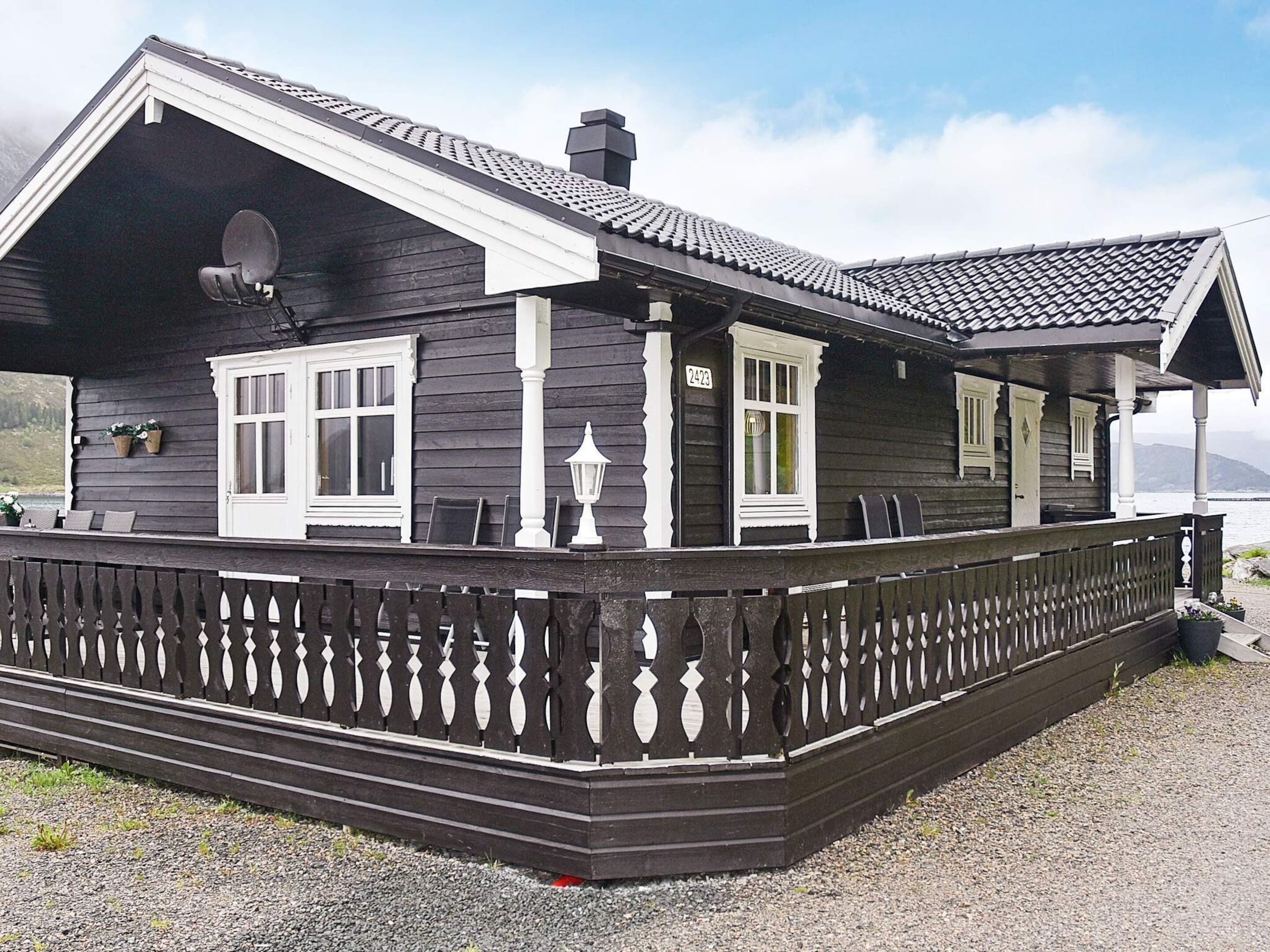A wooden house with a balcony, a satellite dish, and a number 2423 on the door.