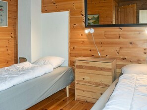 A bedroom with two beds, a wooden dresser, a nightstand, and a mirror on the wall. - Holiday Home in Selje (Stad)