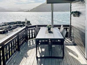 A wooden deck with a table and chairs, overlooking a body of water and hills. - Holiday Home in Selje (Stad)