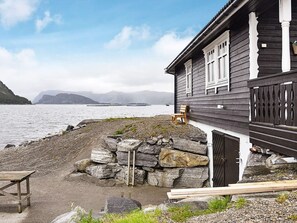 A wooden house with a stone wall and a wooden bench by the water. - Holiday Home in Selje (Stad)