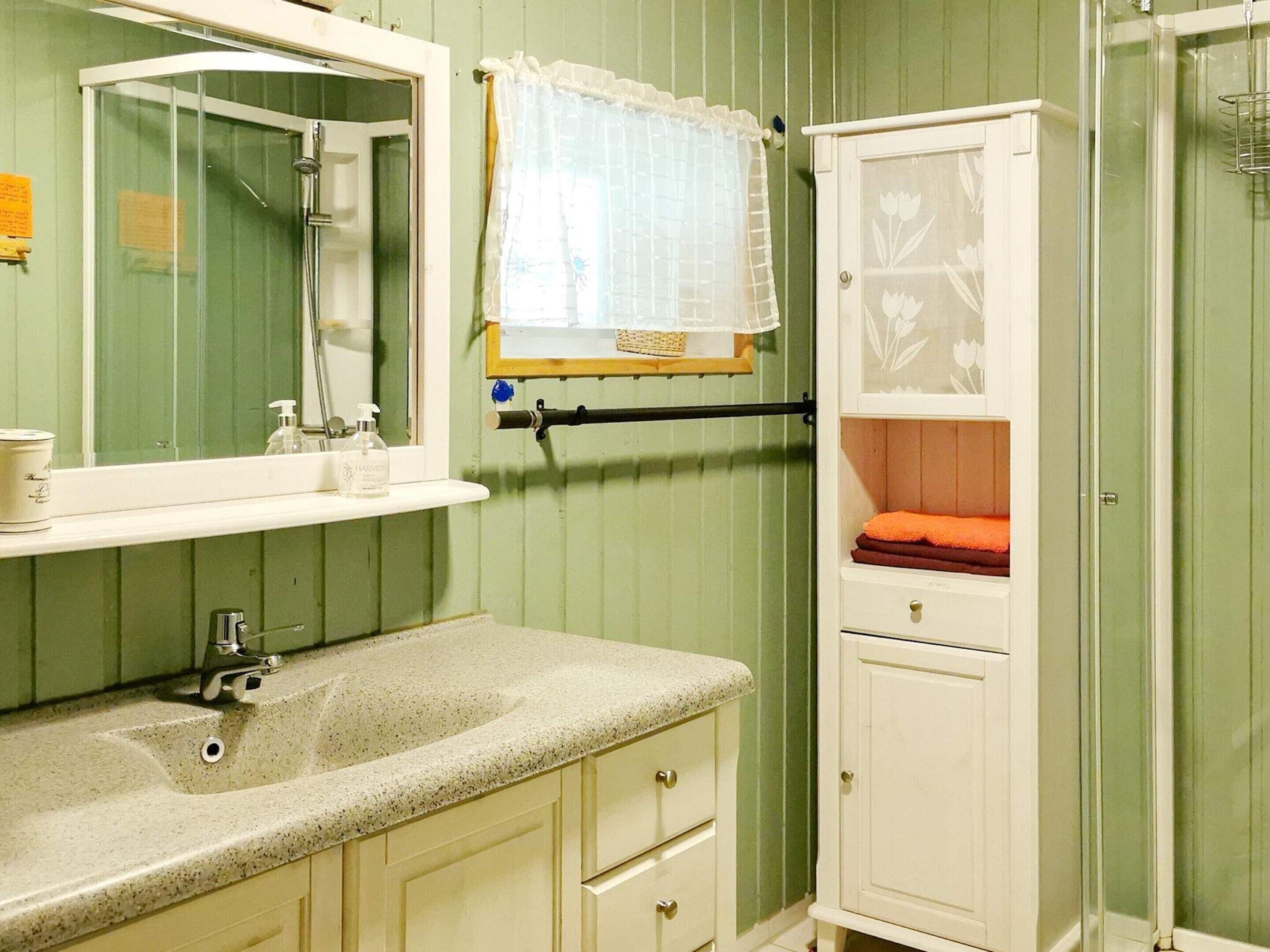 Un baño con lavamanos, espejo y un armario con una toalla.