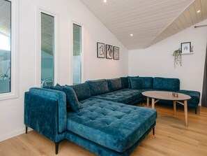 A modern living room with a sectional sofa, a round coffee table, and a large window providing natural light. - 5 Star Holiday Home in Juelsminde (Horsens)