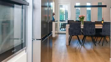 Eine moderne Küche mit einem Edelstahl-Kühlschrank, einem Essbereich mit Tisch und Stühlen sowie Blick ins Freie durch eine Glastür.