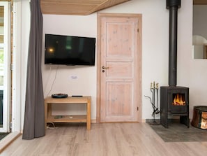 A room with a television mounted on the wall, a wooden door, a fireplace, and a small wooden table with a bowl and remote control. - 5 Star Holiday Home in Juelsminde (Horsens)