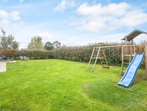 A backyard with a wooden playset, including a slide and swings, surrounded by a well-maintained lawn and hedges. - 5 Star Holiday Home in Juelsminde (Horsens)