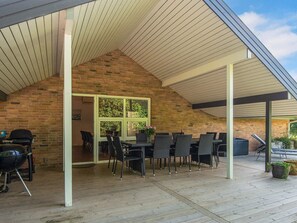 An outdoor patio with a brick wall, a covered seating area with chairs and tables, and a grill. - 5 Star Holiday Home in Juelsminde (Horsens)