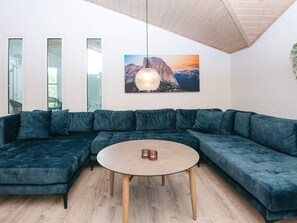 A modern living room with a sectional sofa, a round coffee table, and a painting of a mountain landscape. - 5 Star Holiday Home in Juelsminde (Horsens)