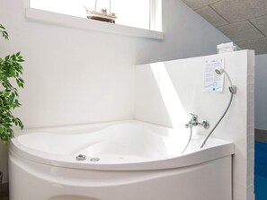 A corner bathtub with a shower head, a plant, and a window. - 5 Star Holiday Home in Juelsminde (Horsens)
