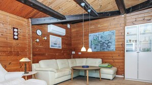 Een gezellig blokhutinterieur met een witte leren bank, een klein rond tafeltje en een houten vloer.