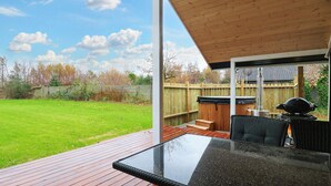 A covered patio with a glass table and chairs, a wooden deck, and a view of a backyard with a wooden fence and trees. - 6 Person Holiday Home in Vaeggerlose-by Traum (Vaeggerlose)