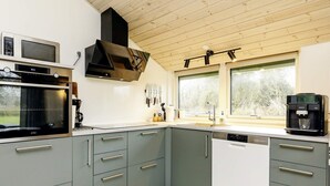 A modern kitchen with grey cabinets, a built-in oven, a coffee machine, and a window with a view of trees. - 6 Person Holiday Home in Vaeggerlose-by Traum (Vaeggerlose)