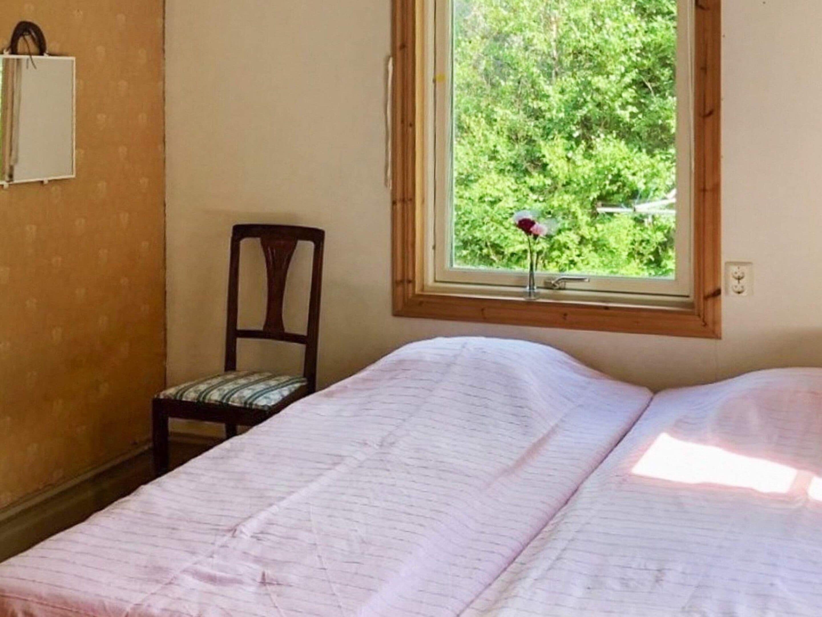 A bedroom with a bed, a chair, a window with a view of greenery, and a wall-mounted shelf.