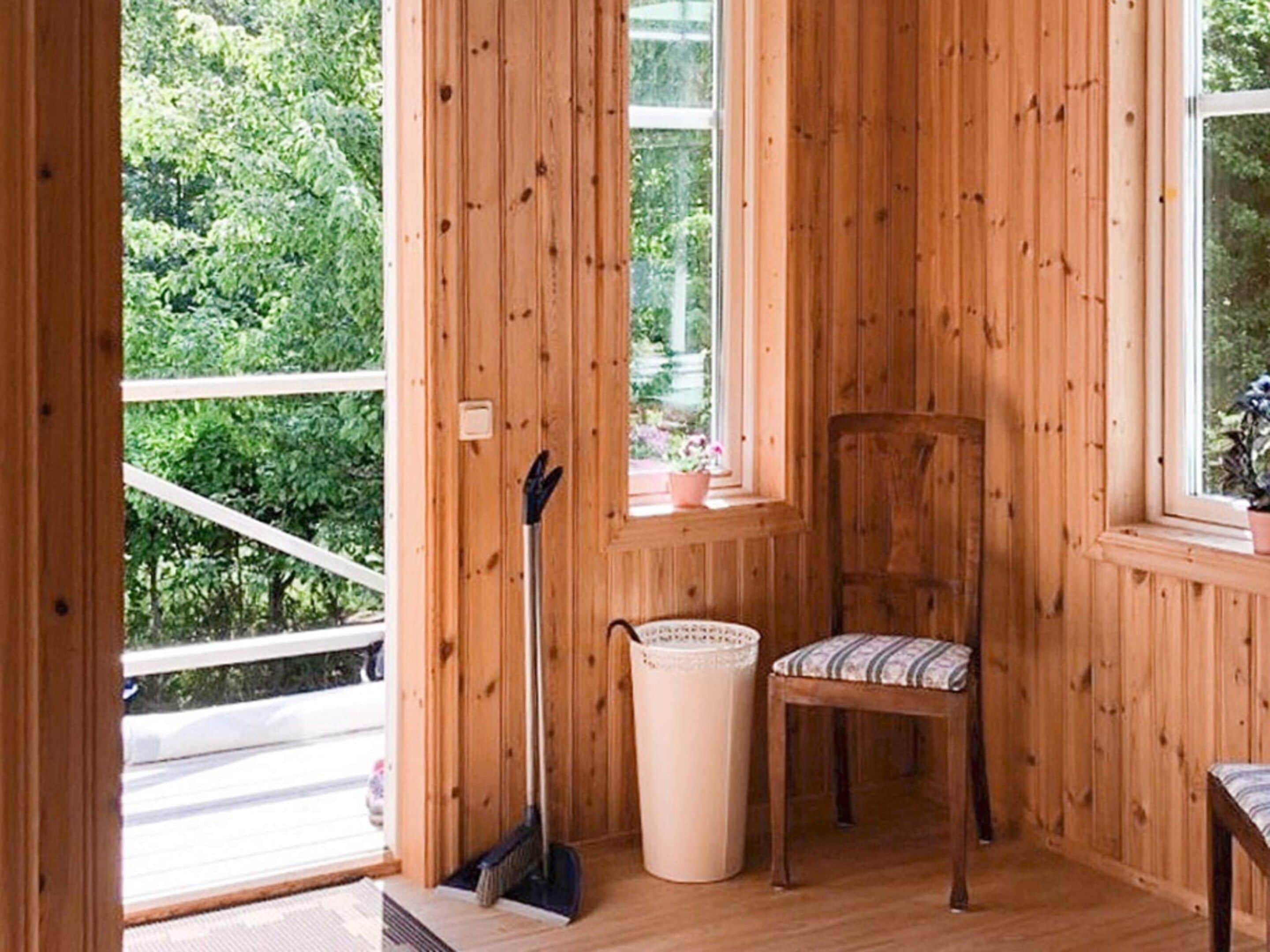 A wooden interior with a chair, a broom, and a window with a view of greenery.